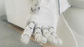 A robot is holding a hand in front of a white wall.
