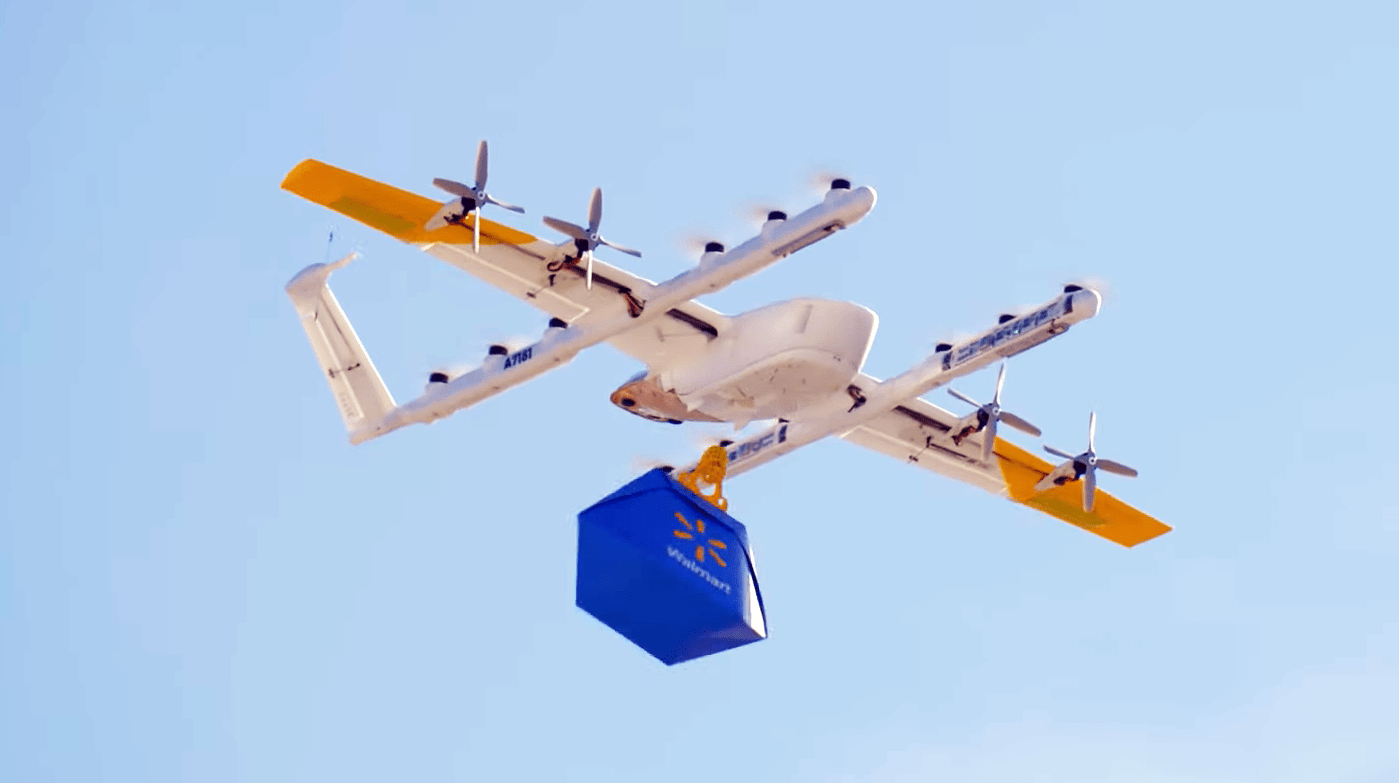 A drone holding a blue and yellow Walmart bag flying in the sky.